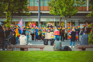 Eine Gruppe Menschen steht als Menschenkette am Paradeplatz mit Schildern und Prideflaggen. Eine Regenbogengirlande ist darüber gespannt.